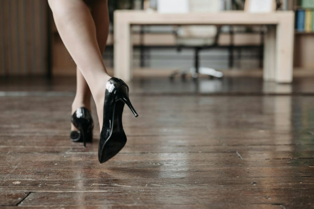 A woman in stylish high heels walks across a polished wooden floor in an office setting.