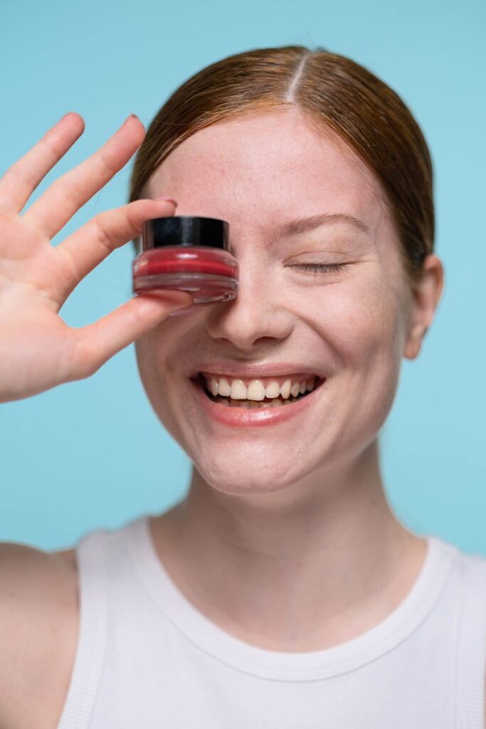 Smiling woman holding lip balm near eye, showcasing beauty product and skincare.