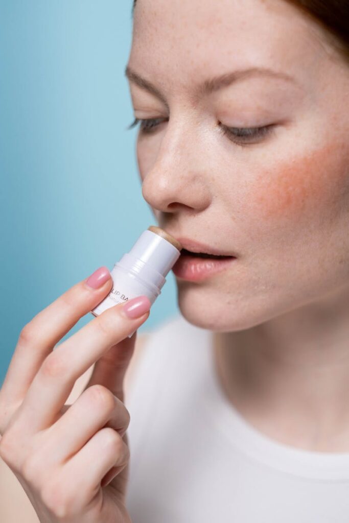 Woman using lip balm during beauty routine in studio setting.