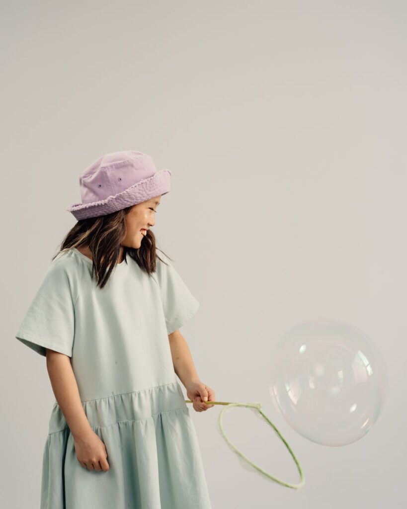 Young girl smiling while creating a large bubble indoors with a neutral background.