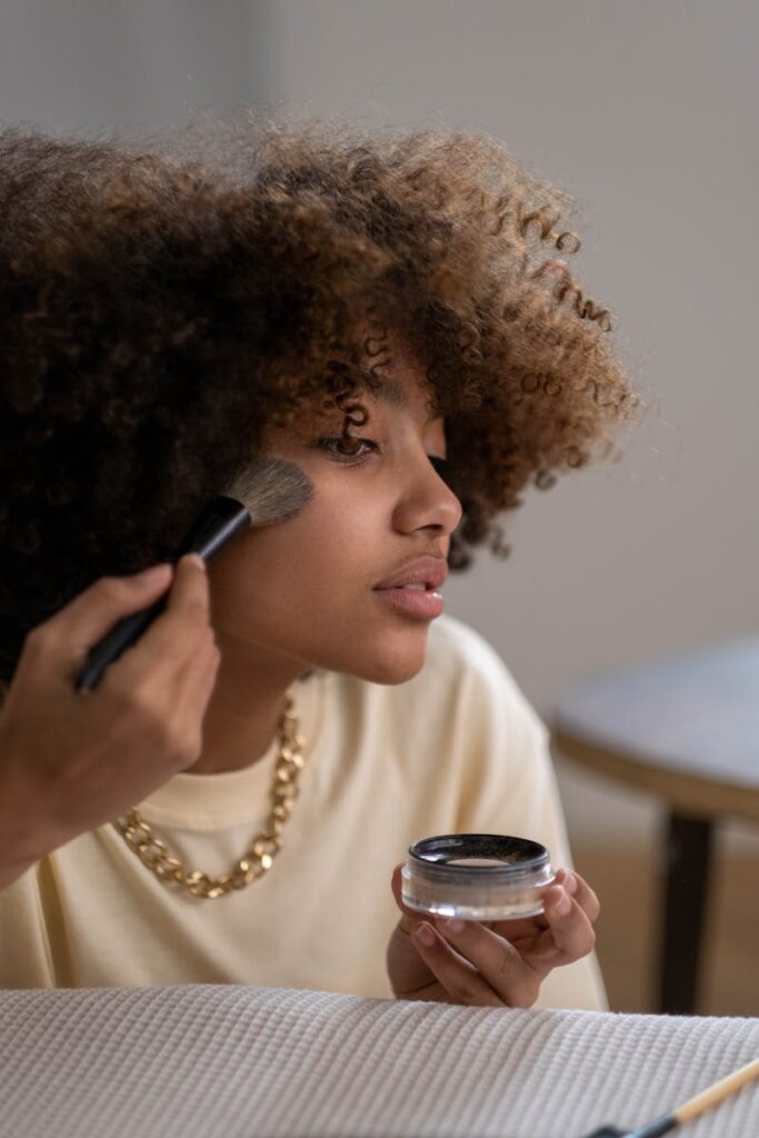 Portrait of a young woman applying makeup indoors, focusing on beauty and self-care.