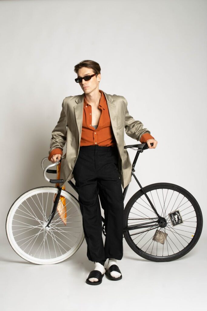 Fashion-forward man in a gray suit, posing with a bicycle against a white studio background.