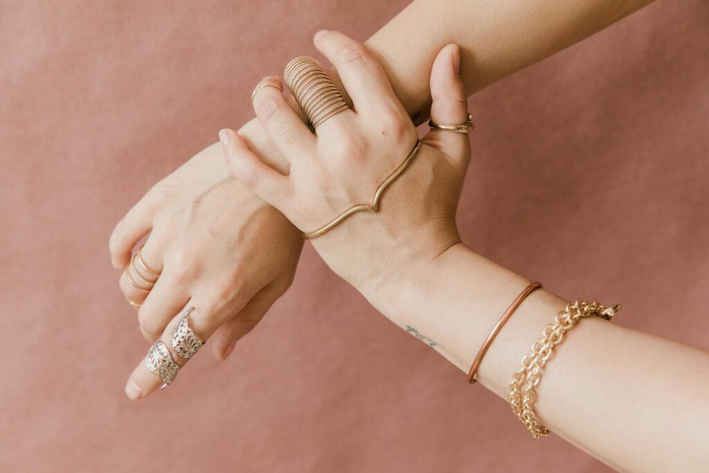 Elegant hands adorned with gold jewelry against a soft pink background, showcasing style and grace.