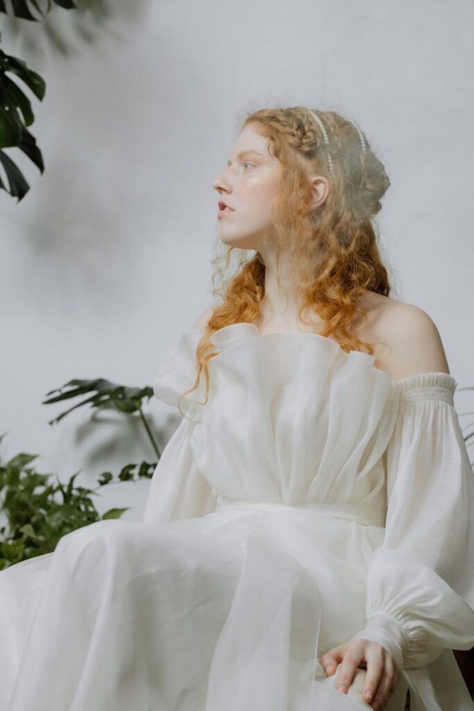 Portrait of a woman in an off-shoulder white dress surrounded by greenery, exuding elegance and grace.