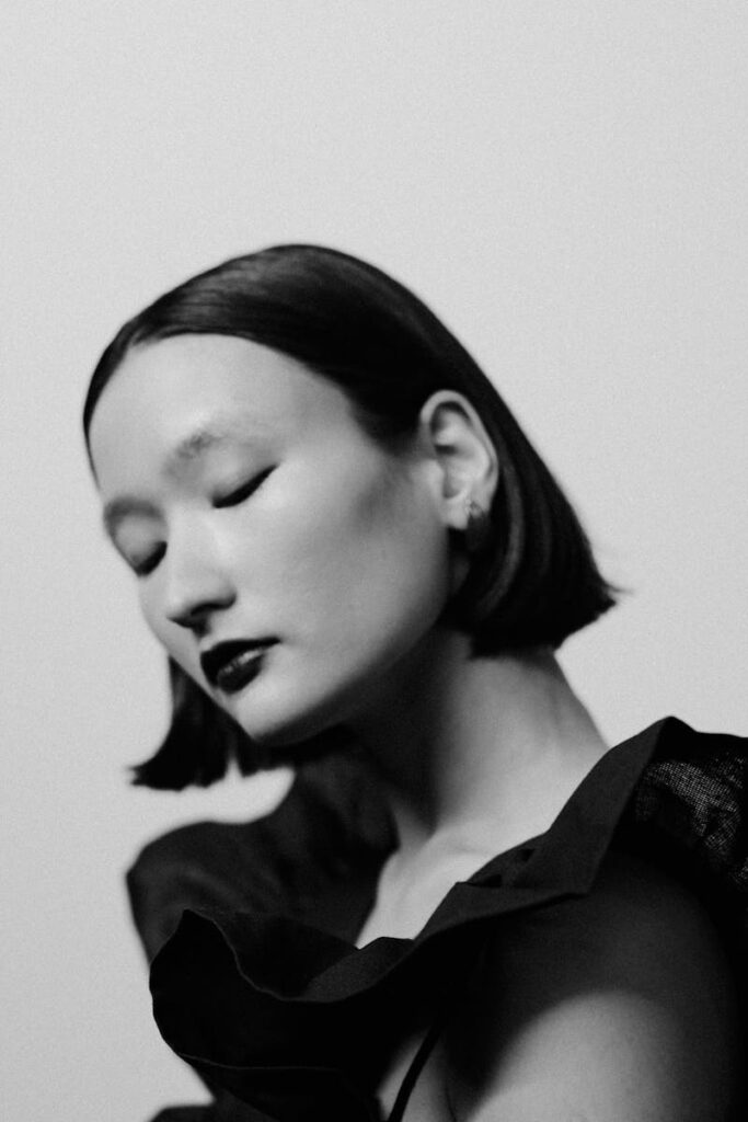 Black and white portrait of an Asian woman with eyes closed in a stylish pose.