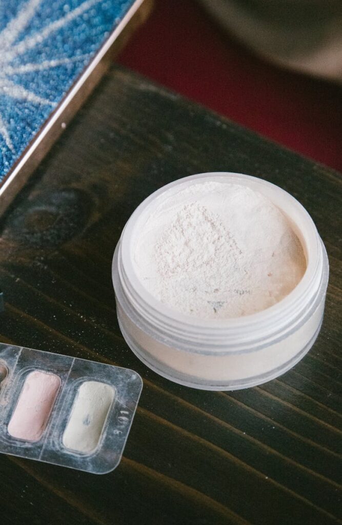 Loose cosmetic powder and colorful makeup palette on a dark wooden table.