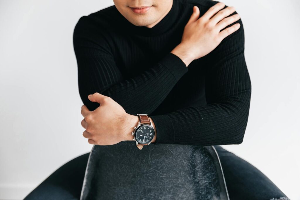 A modern indoor portrait featuring a person in black attire showcasing a leather wristwatch.