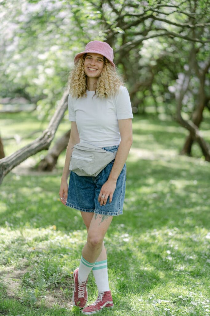 A woman smiling in a casual outfit with a bucket hat in a sunny park.