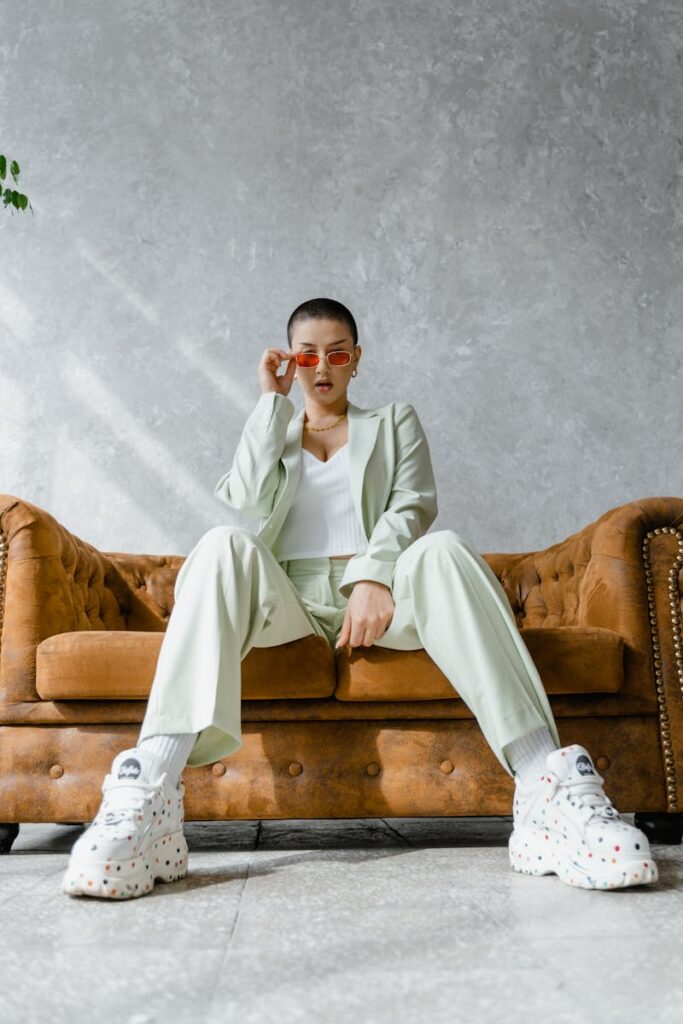 Trendy woman wearing a mint suit and sneakers, sitting confidently on a vintage couch indoors.