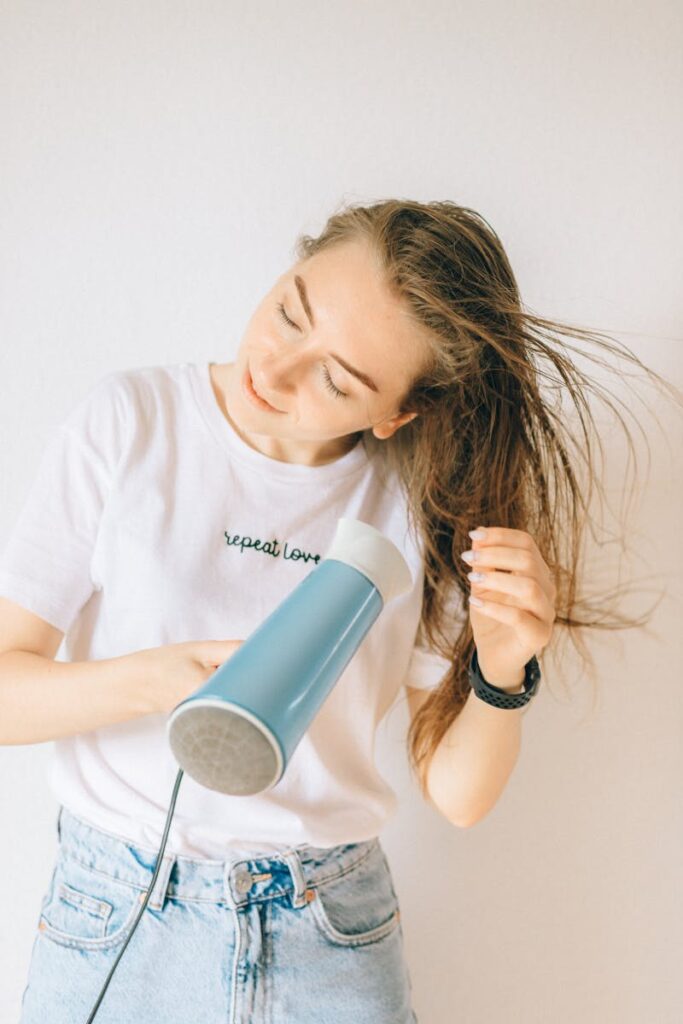 A young woman using a hair dryer to dry her long brown hair indoors.