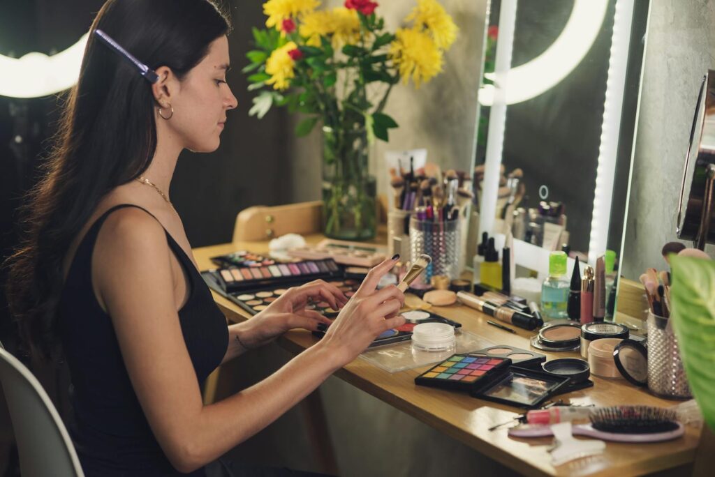 A woman prepares her makeup in a stylish indoor setup, surrounded by beauty products.