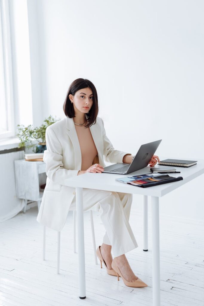 Elegant businesswoman in a white blazer working on a laptop in a bright, modern office.