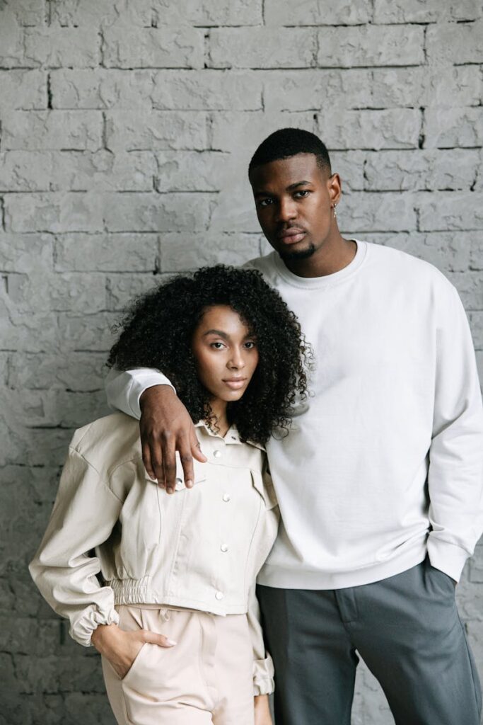 Fashionable couple in casual attire standing by a textured wall.