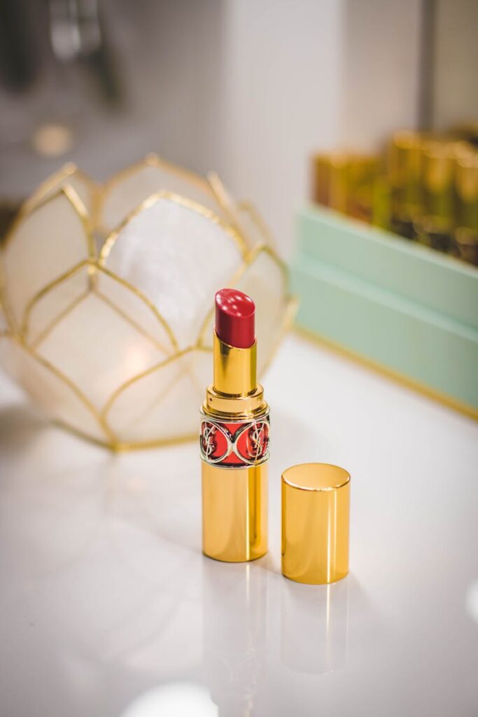 Luxurious red lipstick in gold tube on a reflective makeup table, epitomizing elegance and beauty.