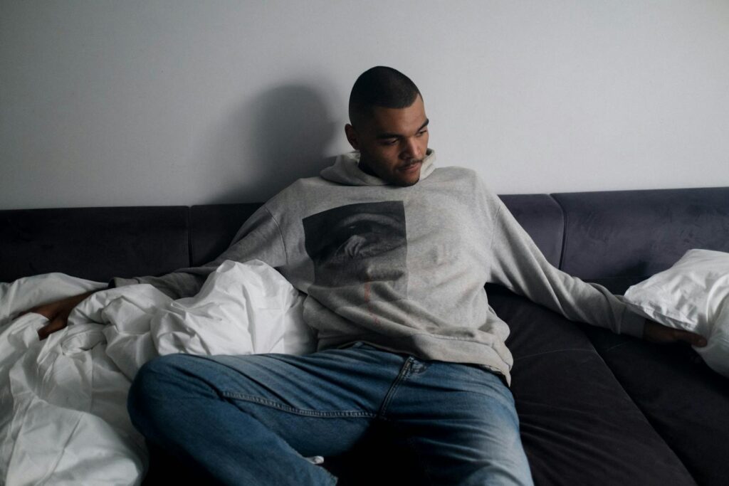 A man in casual clothing sitting on a sofa, appearing thoughtful and introspective.