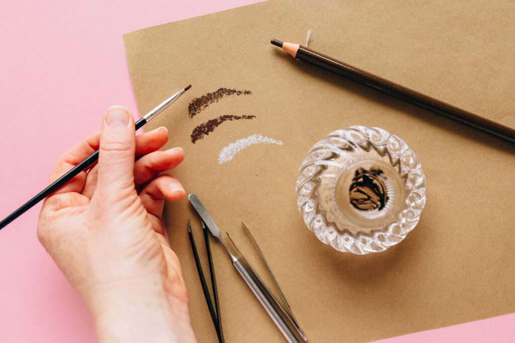 Close-up of a hand holding a brush with makeup tools on colored paper.