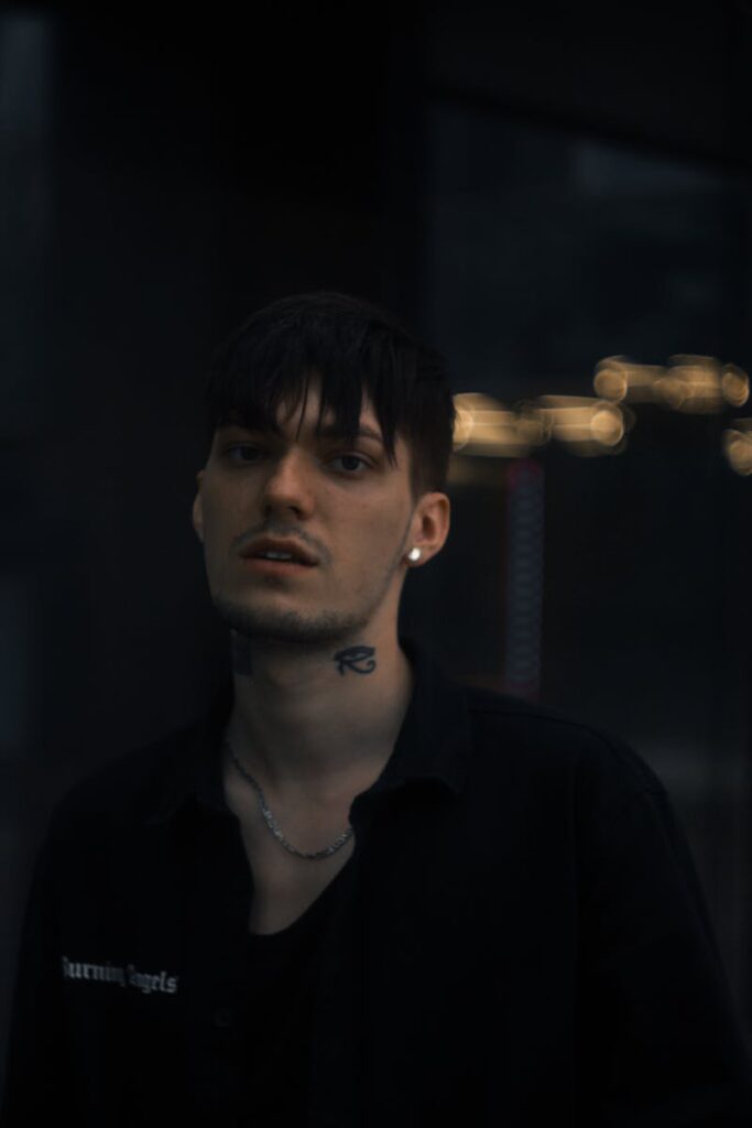 Dark portrait of a tattooed man with a necklace at night, showcasing moody and edgy style.