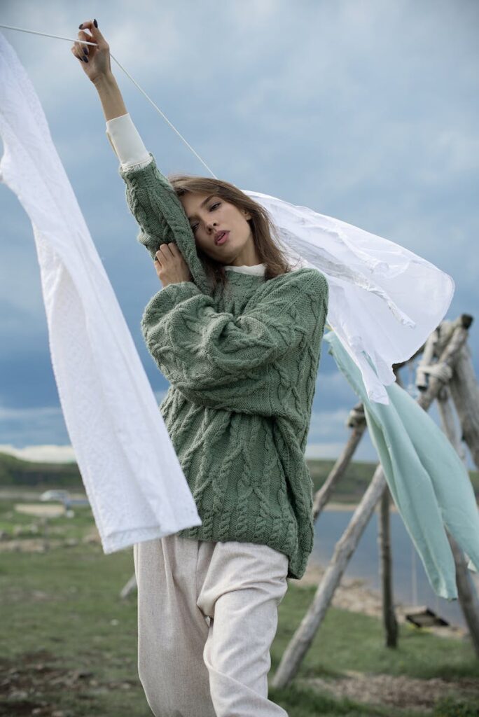 Woman in green sweater posing near clothesline outdoors.