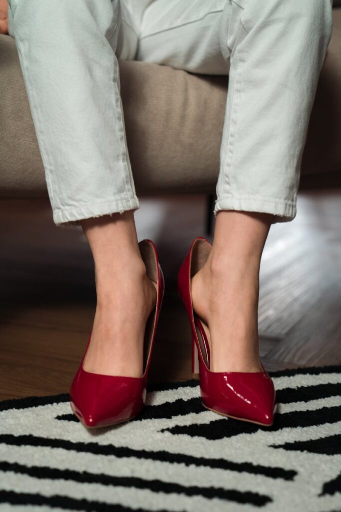 Close-up of red high heels paired with white jeans on a patterned carpet.