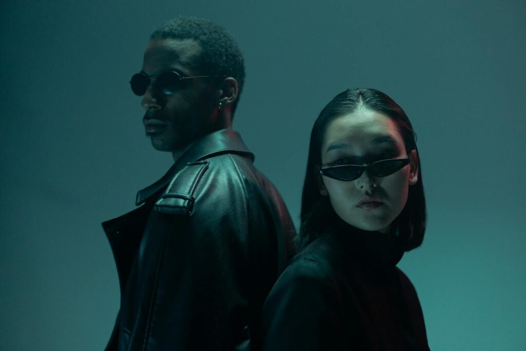 Two models in stylish black attire with sunglasses in a conceptual portrait.