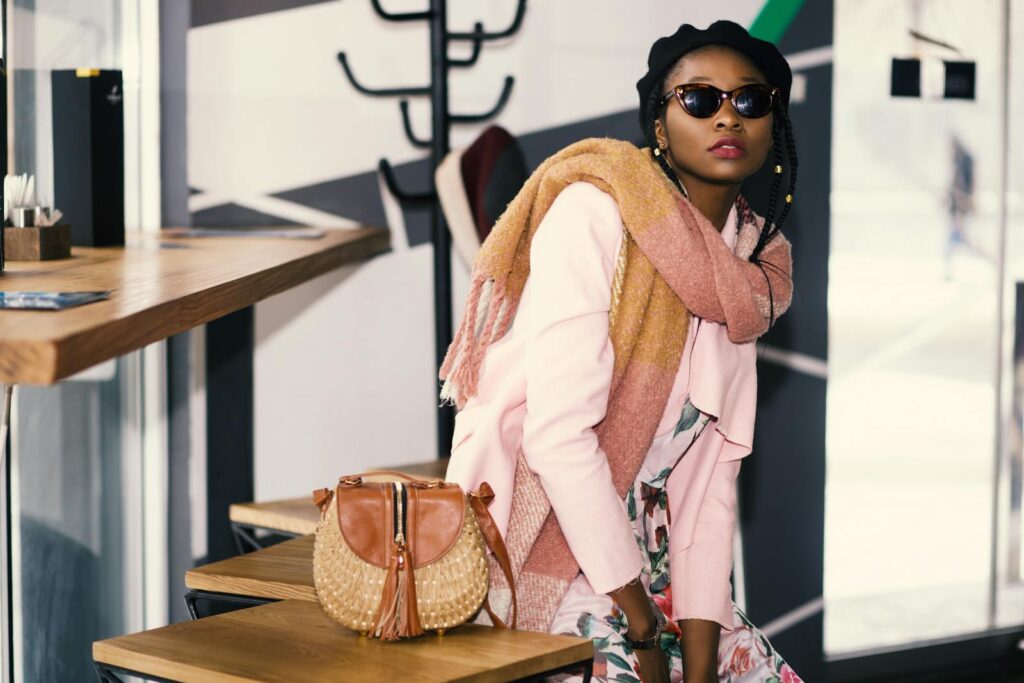 Chic African woman with sunglasses and scarf sitting indoors beside a stylish bag.