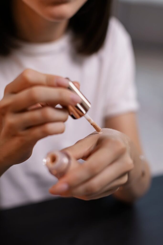 A woman's hands testing liquid foundation with a cosmetic applicator indoors.