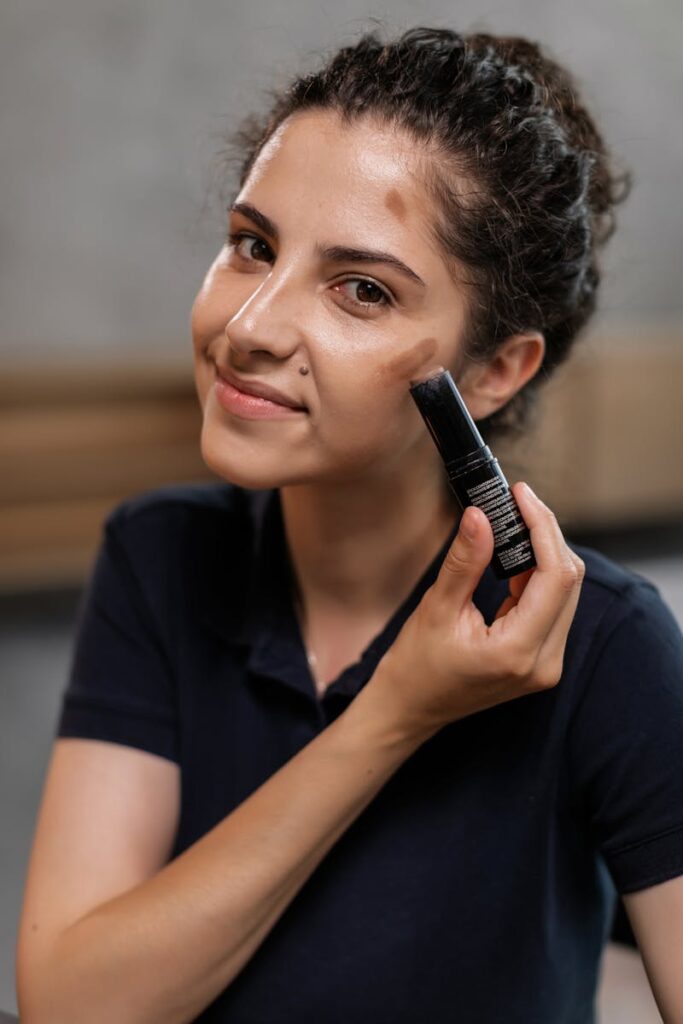 Woman demonstrating makeup application with concealer, enhancing natural beauty indoors.