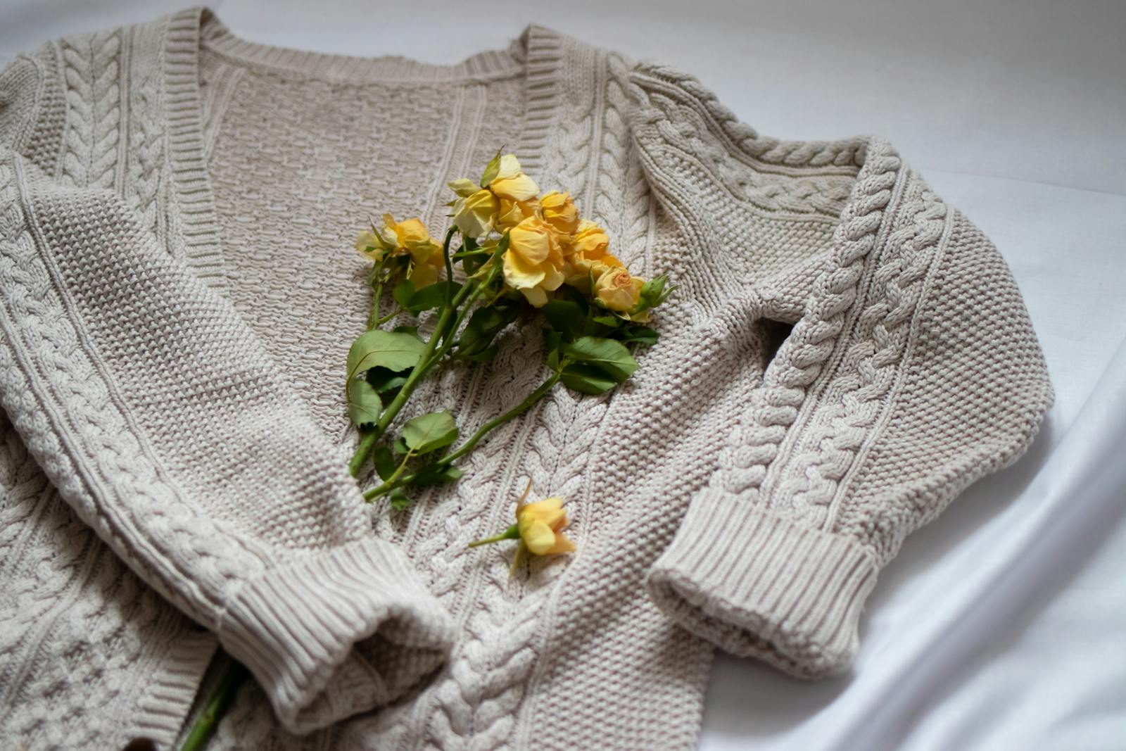 A beige cable-knit cardigan adorned with delicate yellow roses, evoking warmth and coziness.