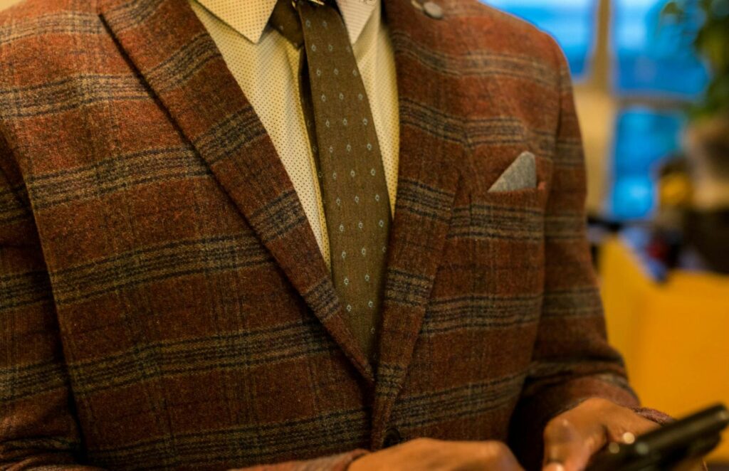 Close-up of an adult wearing a stylish plaid jacket with a polka dot tie, showcasing fashion and texture.