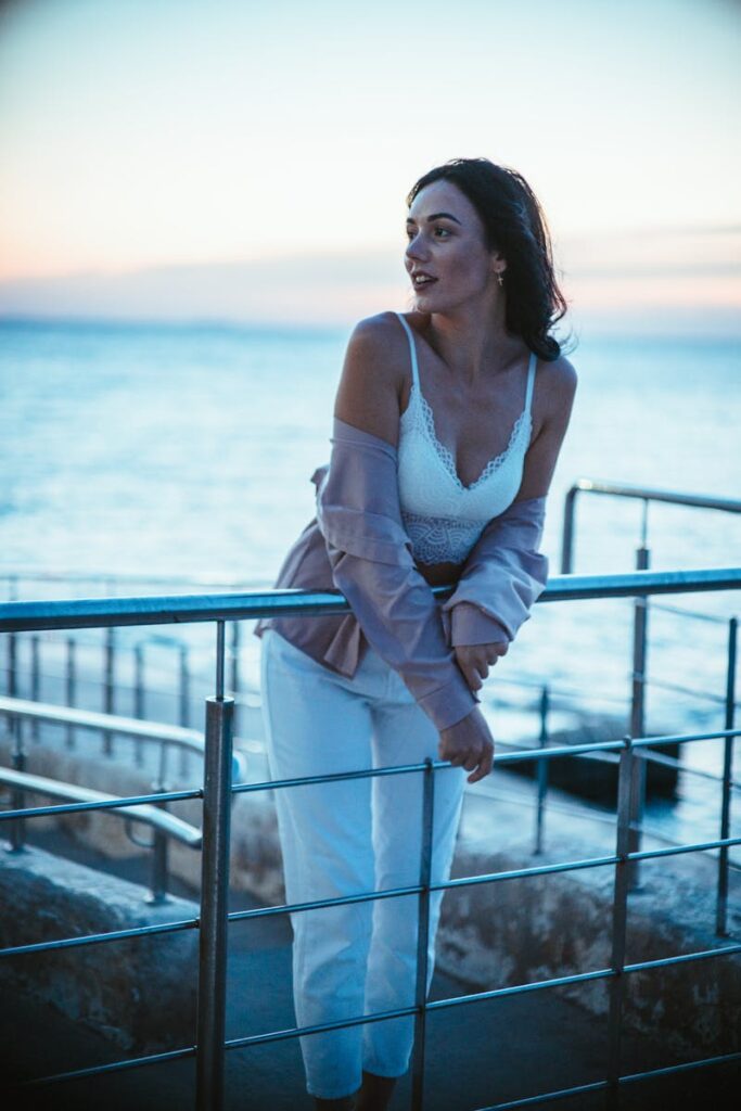 A woman in stylish attire poses by the seaside during a tranquil twilight.