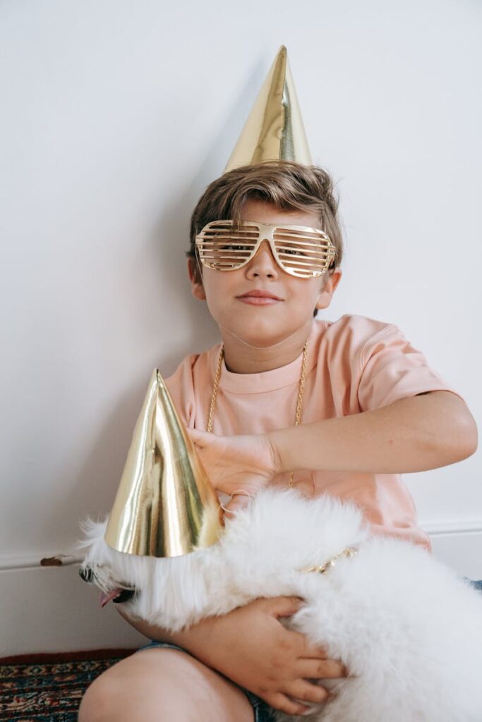 Boy and Maltese dog in party hats and sunglasses enjoying a fun indoor celebration.