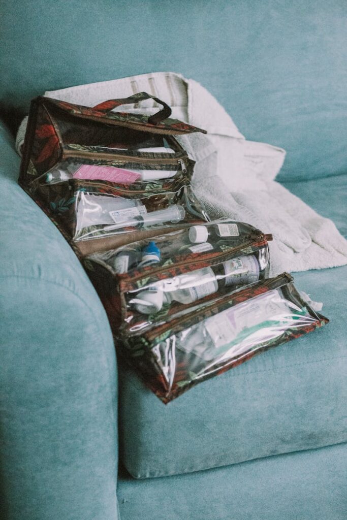 Clear travel bags with toiletries neatly arranged on a teal sofa indoors.