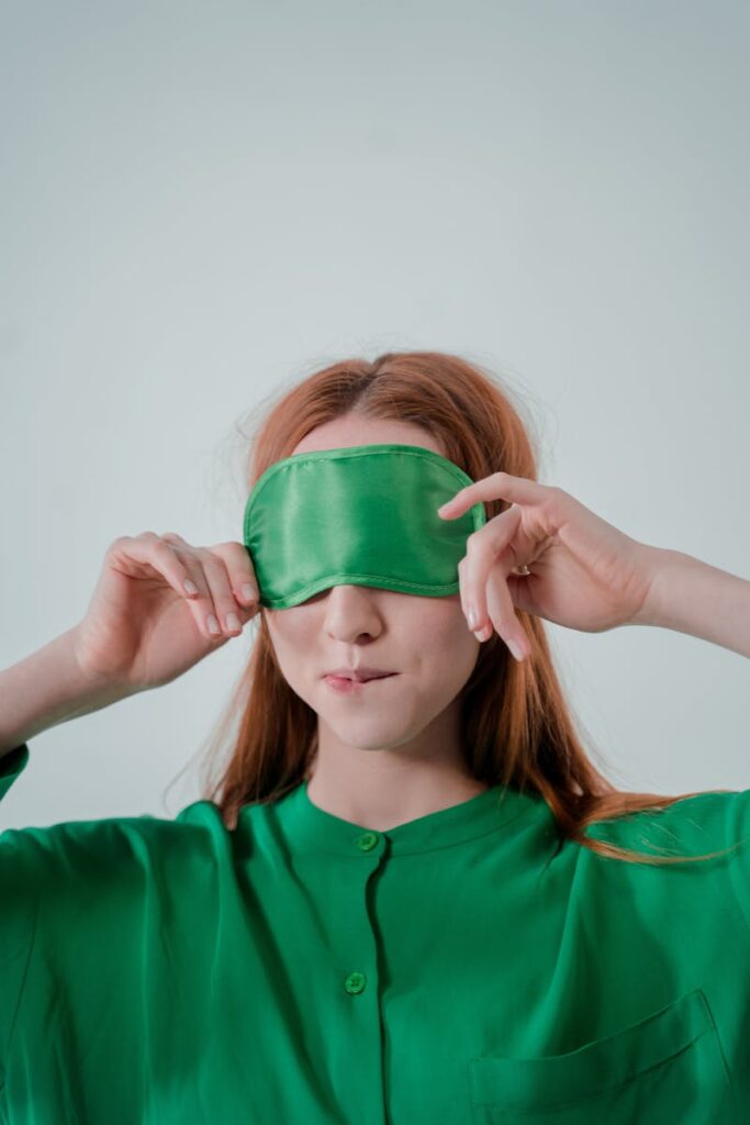 Close-up of a woman with a green sleep mask against a light background, enjoying relaxation.