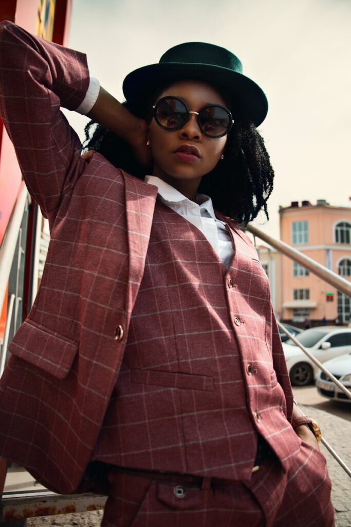 Confident woman in plaid suit and sunglasses posing outdoors in a vibrant urban setting.
