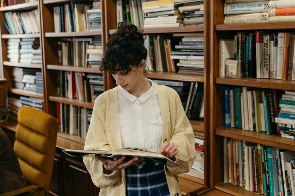 A young woman reading inside a library, surrounded by shelves of books, ideal for education themes.