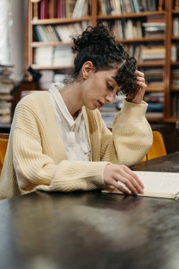 Young woman in a yellow cardigan engrossed in a book at a library.