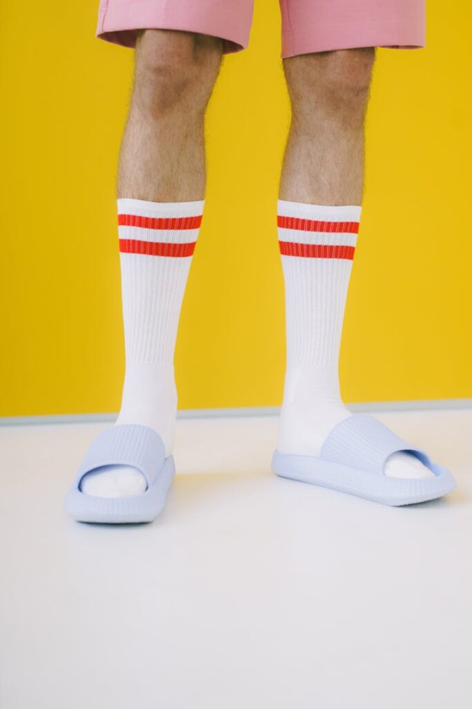 Stylish men's legs in socks and sandals against a vibrant yellow wall.