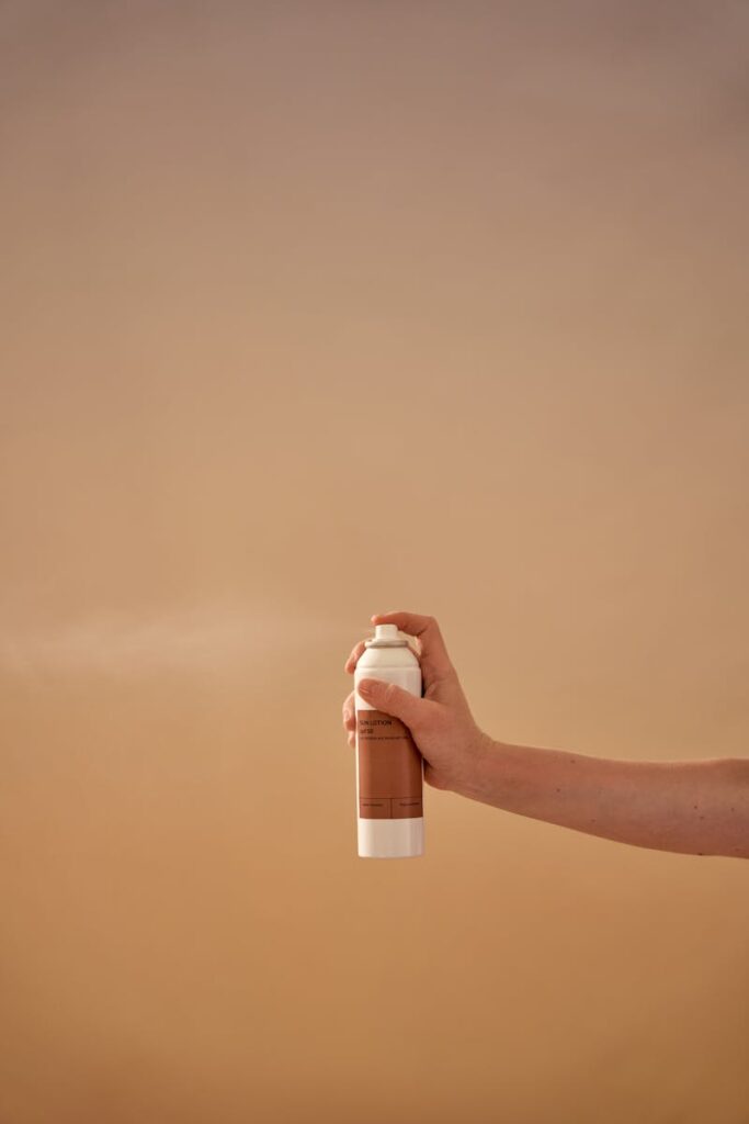 A clean studio shot of a hand holding a sunscreen spray bottle with a neutral background.
