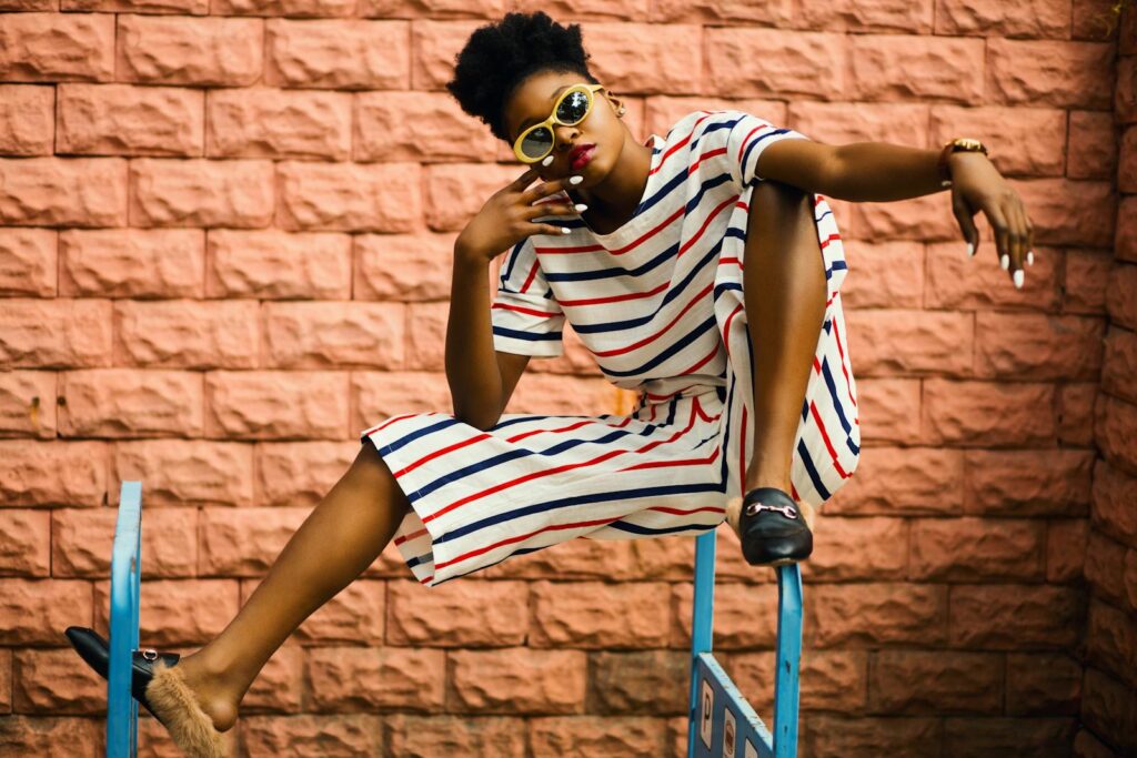 Fashionable woman wearing stripes and sunglasses poses against brick wall.