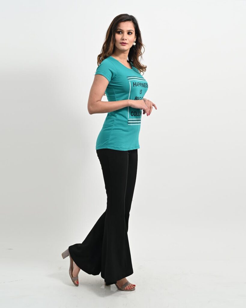 Elegant woman posing in stylish teal top and black bell bottom pants.