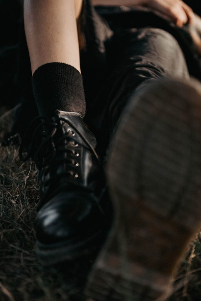 Artistic close-up of black leather boots worn outdoors, emphasizing shiny leather and rugged sole.