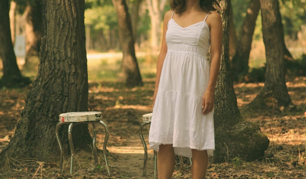 woman in white spaghetti strap dress standing in front of white stool