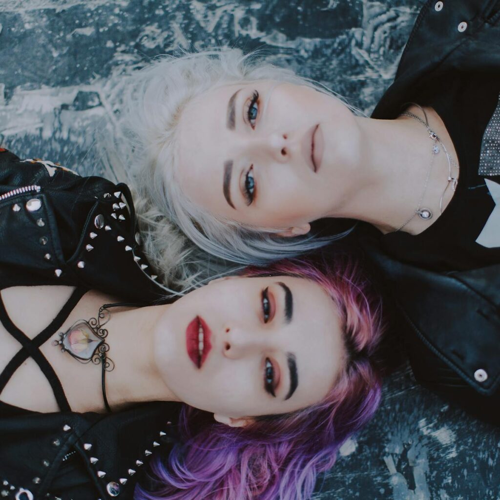 Stylish portrait featuring two women with striking hair colors and edgy fashion in an artistic pose.