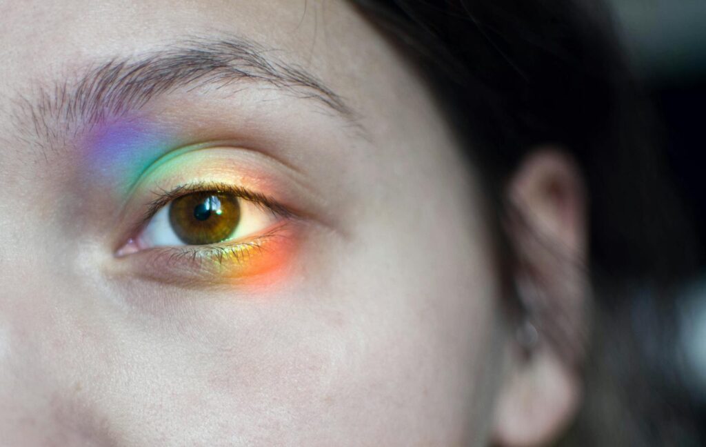 A macro shot showing a close-up of a young woman's eye with a rainbow reflection effect.