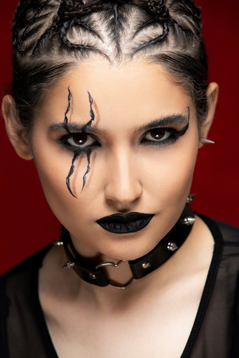 Gothic portrait featuring artistic makeup with black lipstick and braided hair against a red background.