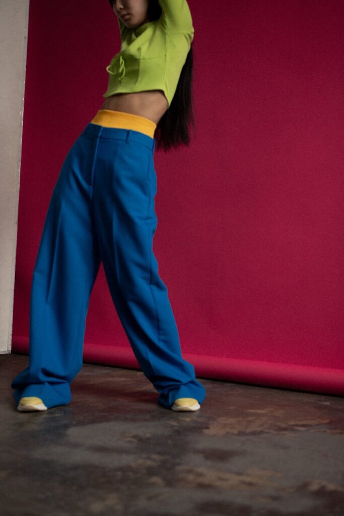 Woman in vibrant outfit posing against red backdrop, showcasing modern fashion trends.