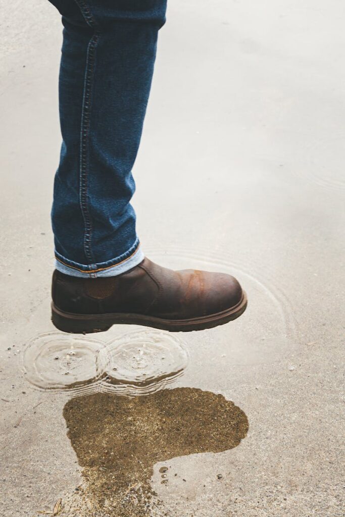 Close-up of a man's brown leather boots stepping into a puddle with reflected leg. Perfect for fashion and lifestyle themes.
