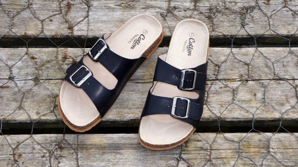 Black leather buckle sandals on a wooden surface, perfect for casual summer fashion.