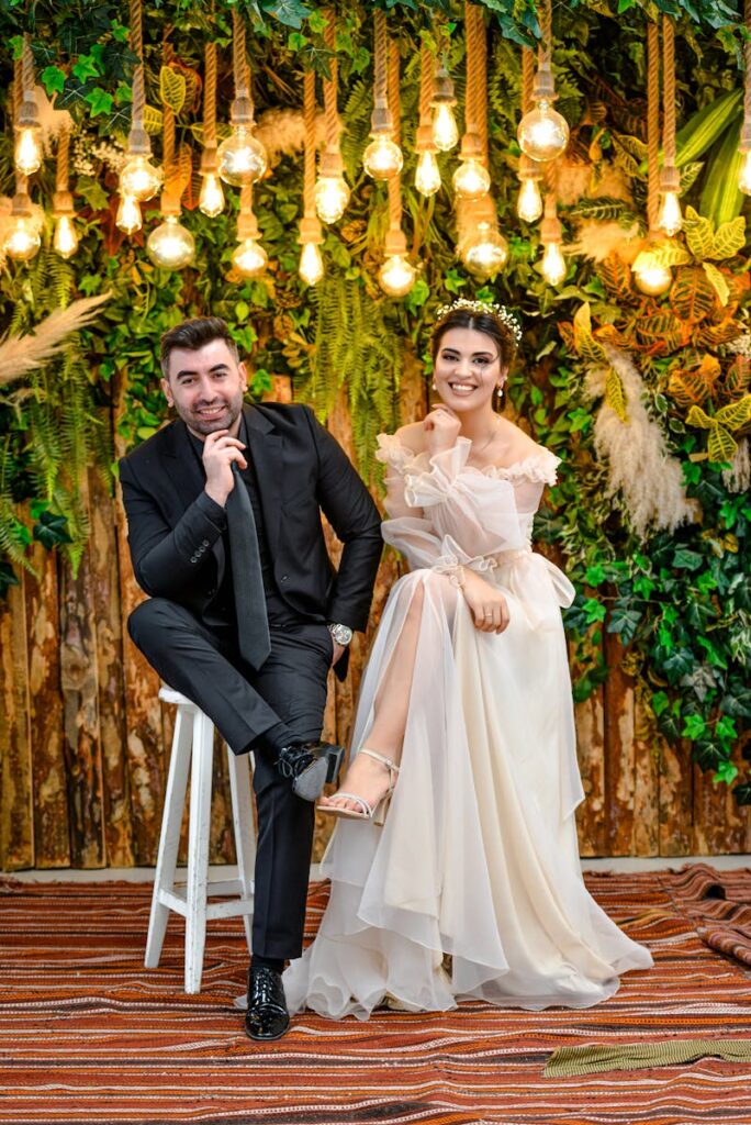Stylish bride and groom posing against rustic, illuminated backdrop, exuding joy and elegance.