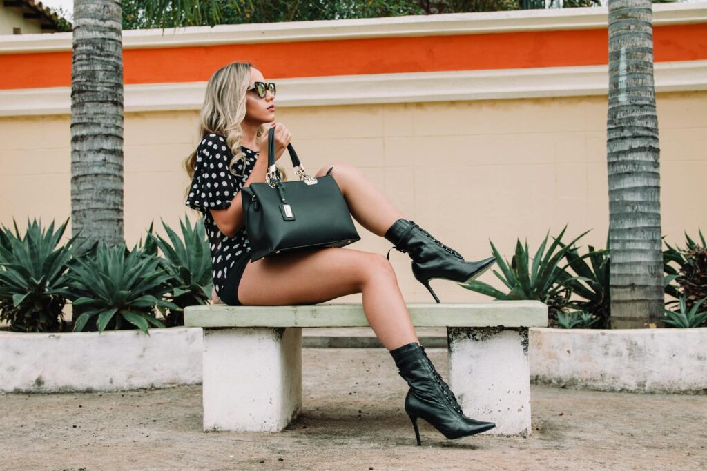 Fashionable woman in boots and sunglasses poses on a bench outdoors.